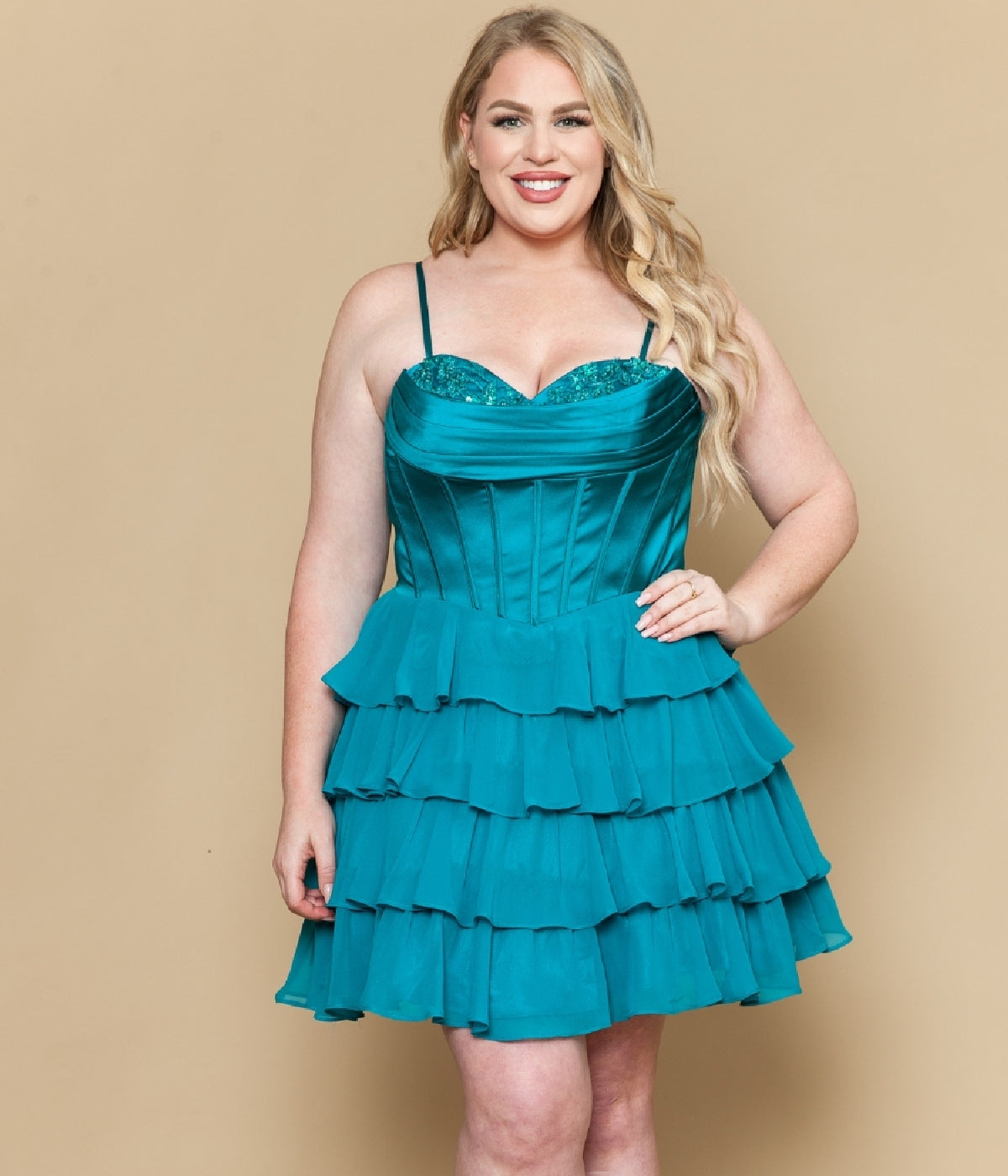 A woman wearing the Short Plus Size Homecoming Dress: Poly USA W1196 in teal, featuring spaghetti straps and a chiffon A-line skirt, stands against a beige background and smiles at the camera.